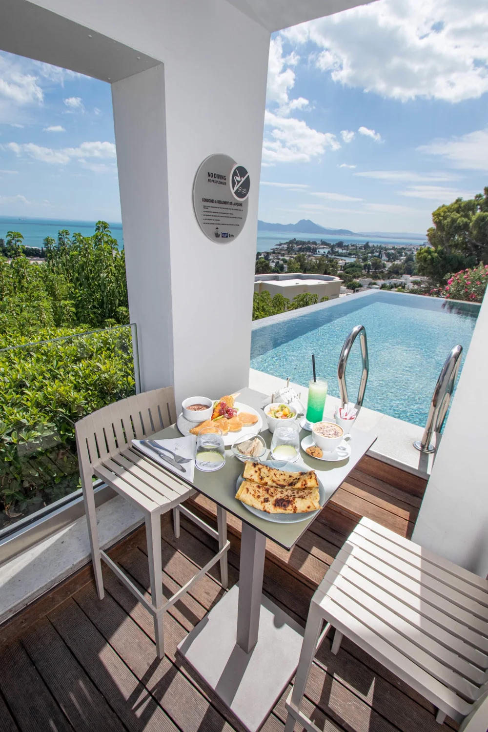 A breakfast table laid on the deck beside the infinity pool, the Bay of Carthage below