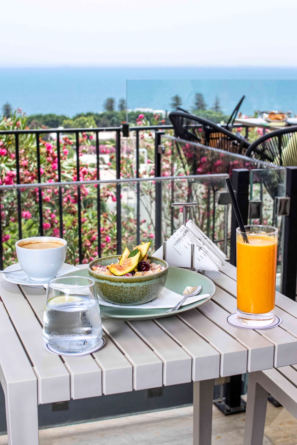 A café crème and a basket of fruit, bougainvillaea and the sea behind