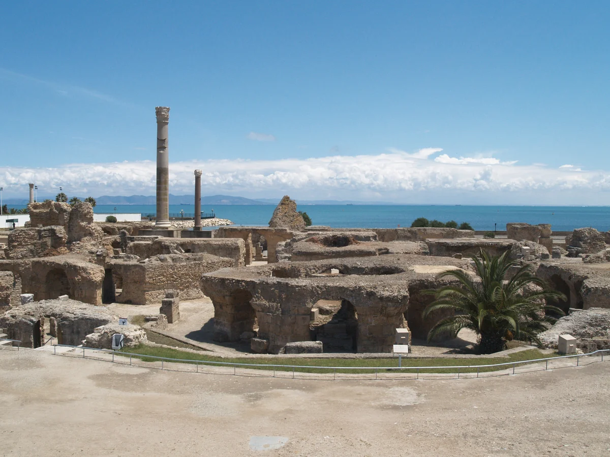 The Baths of Antoninus: ruined vaulted substructures, a standing column and the sea beyond, under a blue sky