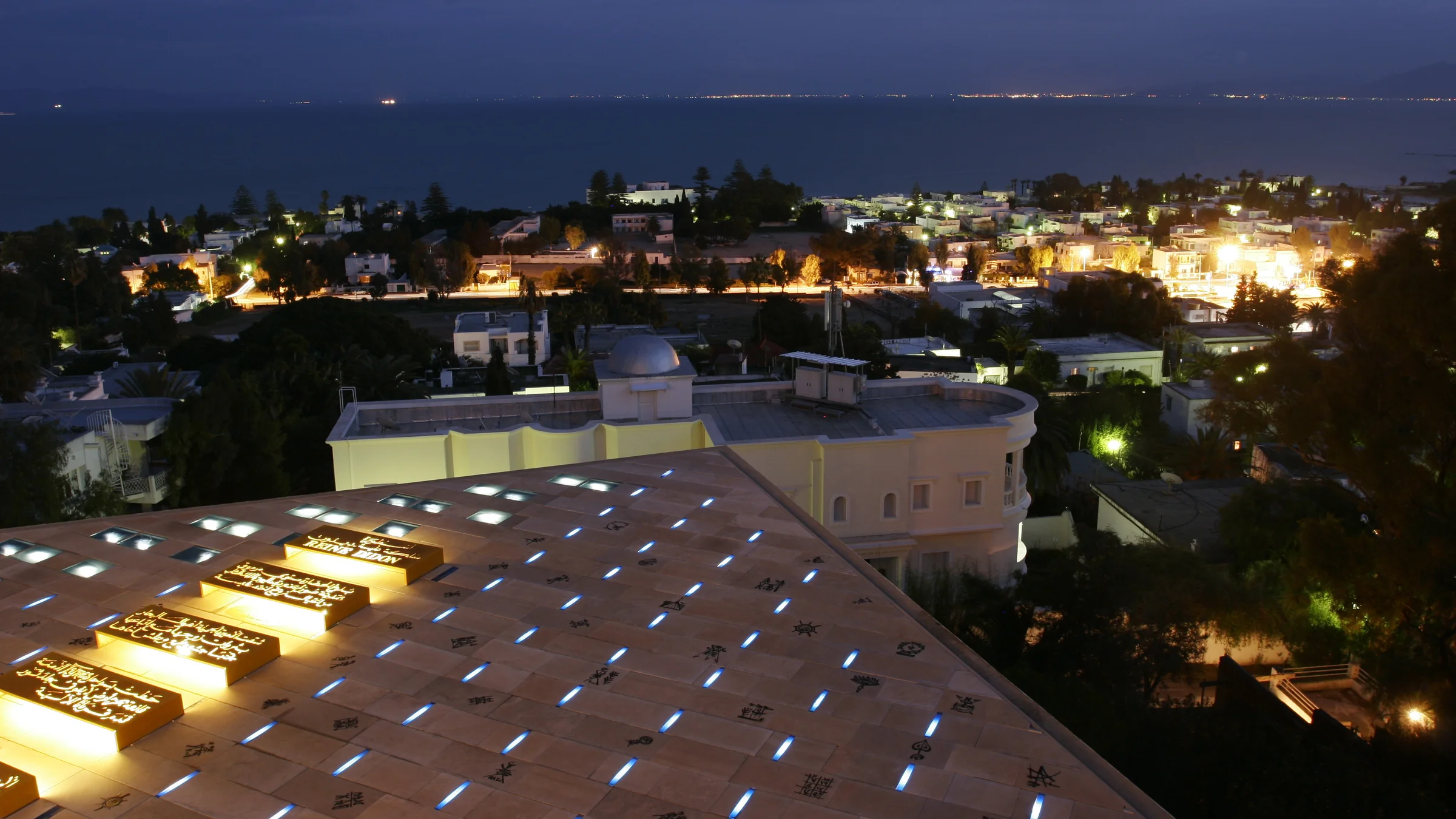 The bay of Carthage at nightfall, seen from the villa's roof, with lit calligraphy in the foreground