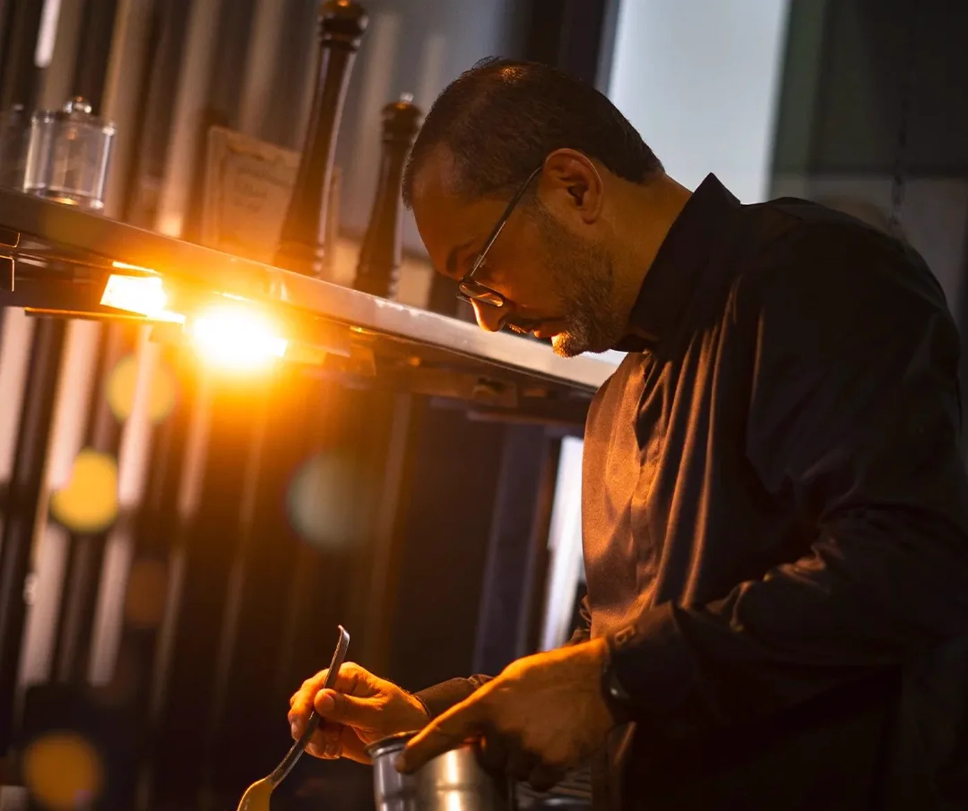 The chef at the pass, in the golden light of the kitchen, intent on plating a dish