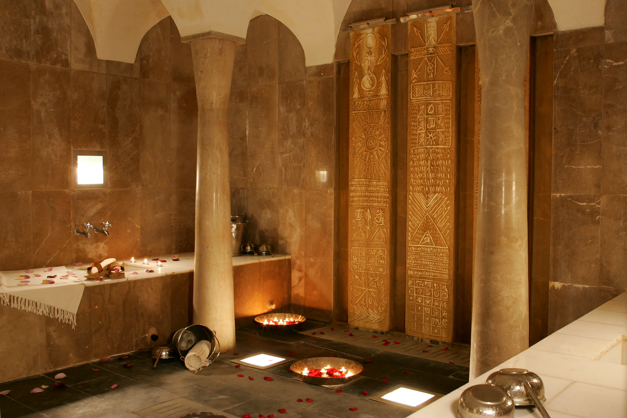 The marble hammam at Villa Didon: columns, panels carved with gilded motifs, copper basins holding floating candles, rose petals strewn across the floor
