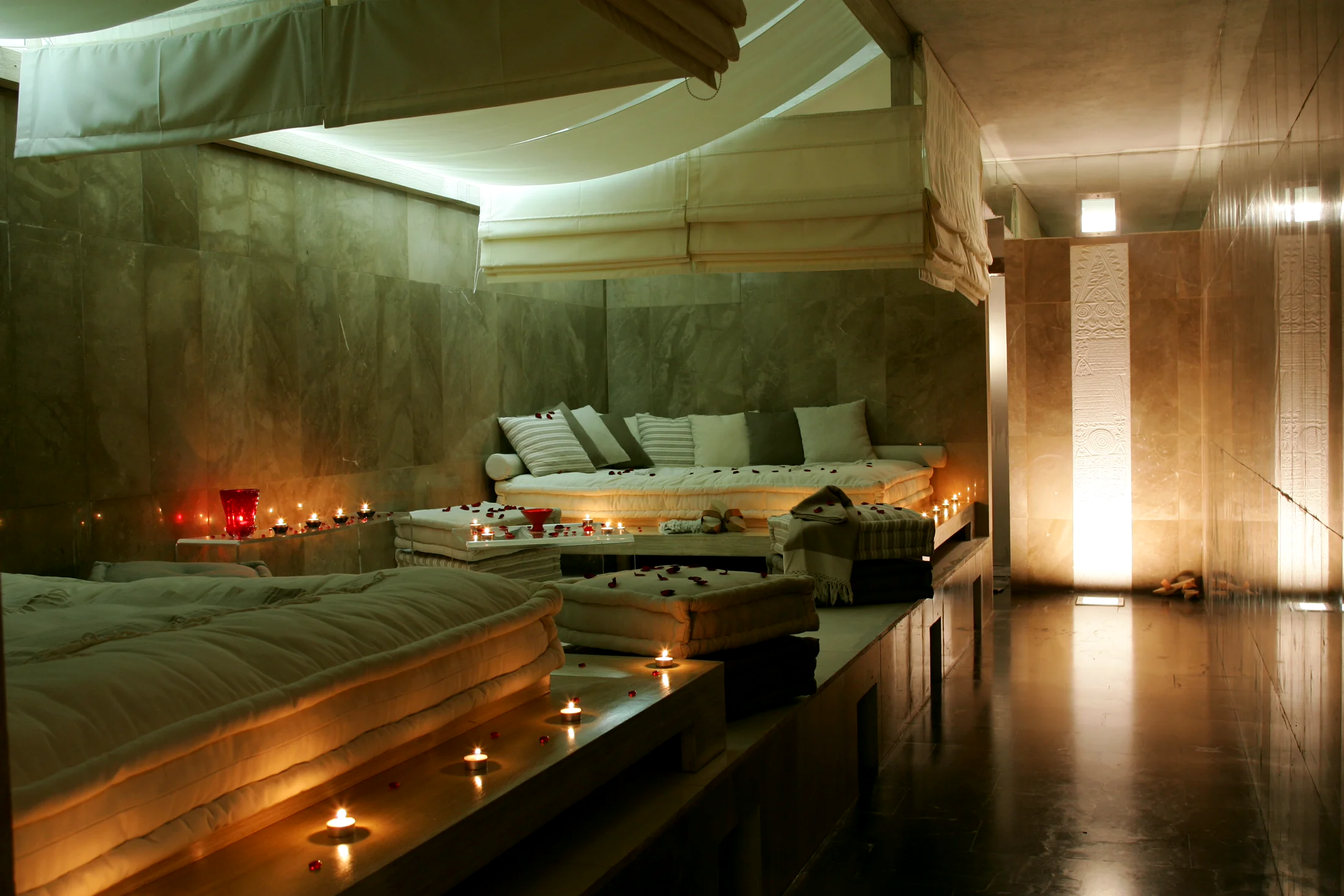 The relaxation room at the Villa Didon spa: low mattresses and cushions, candles and rose petals, marble walls bathed in warm light